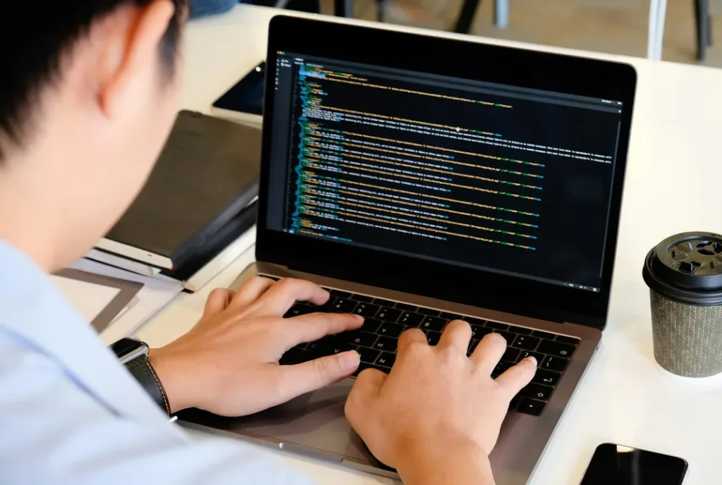 A developer writing code on a laptop at a bright desk