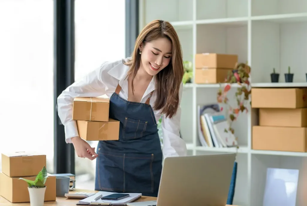 A small business owner packing online orders beside a laptop